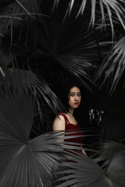 站在绿色植物旁边的穿着红色吊带衫的女人